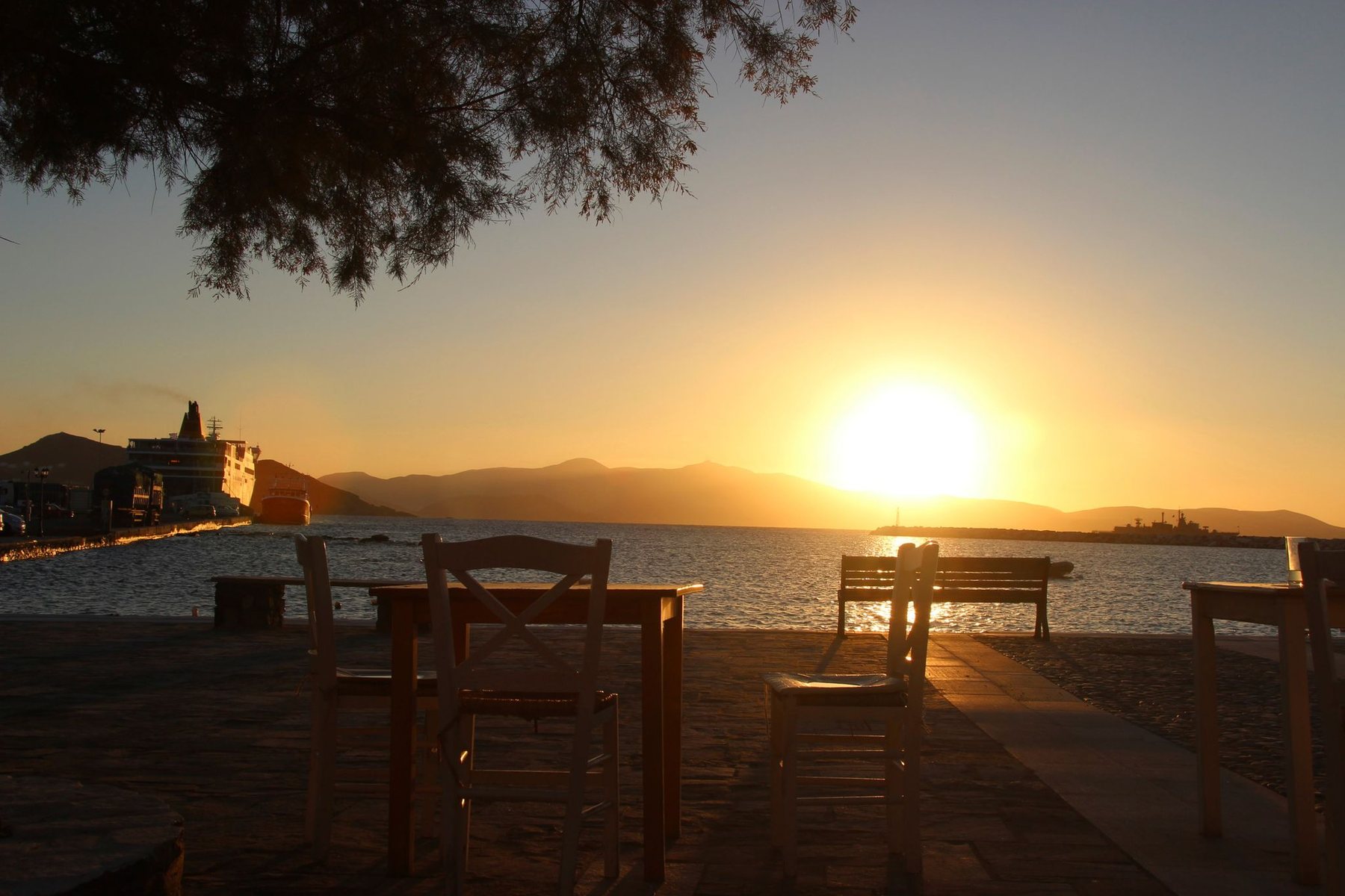 Chairs on a quay at sunset, looking across the water to the hills
