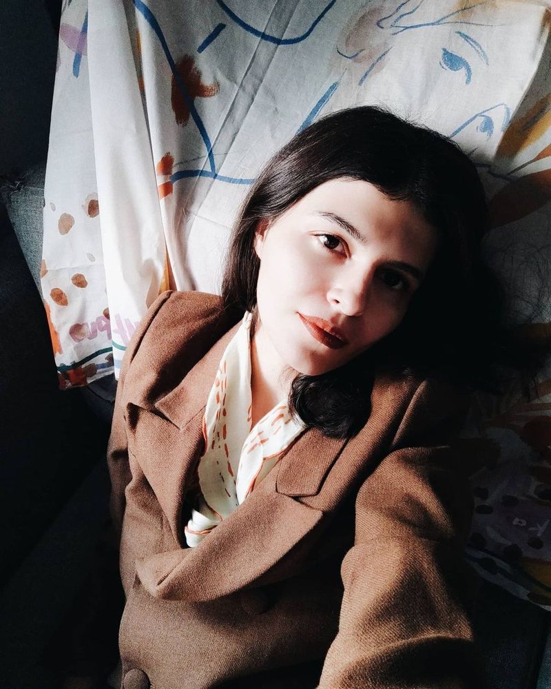 Tuğçe resting her head on her hand, in a brown jacket